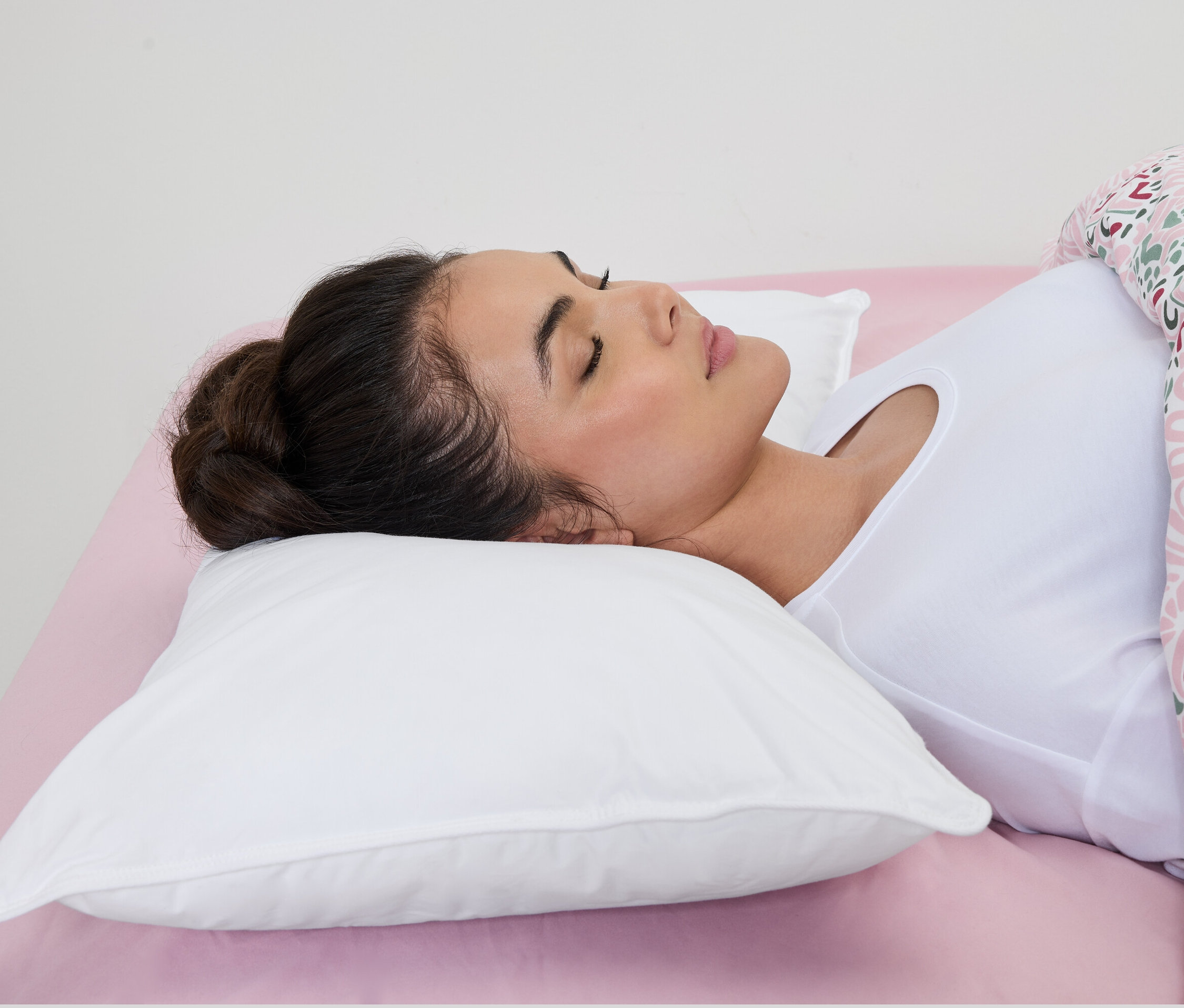 Nő alszik egy fehér irisette® vízzel töltött párnán rózsaszín lepedőn.