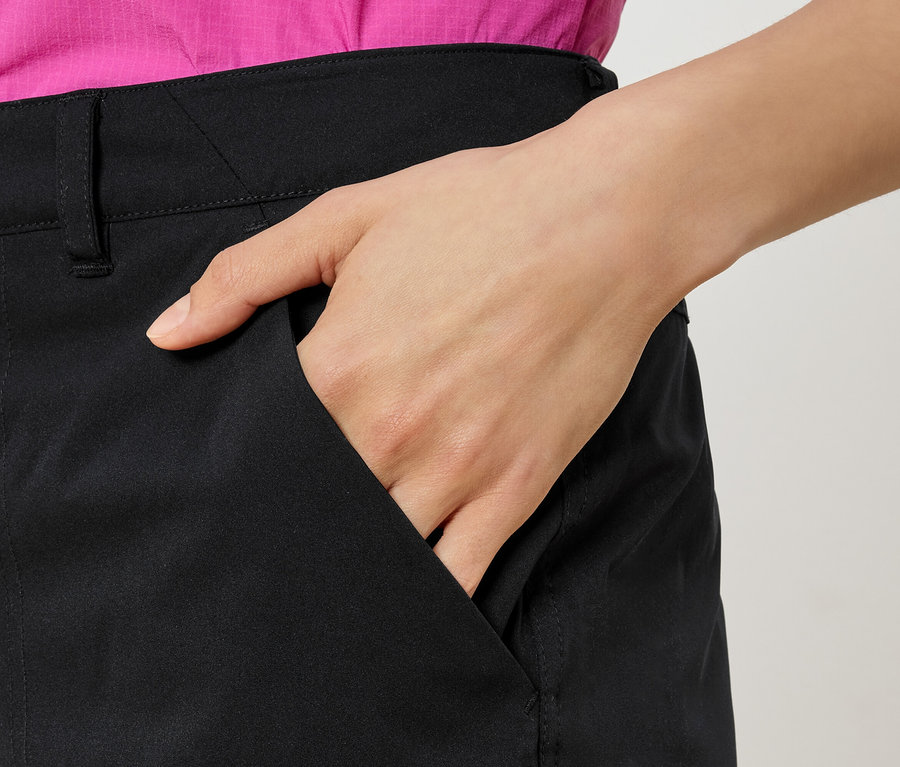 Nő a kezével a fekete nadrág zsebében, rózsaszín ingben.