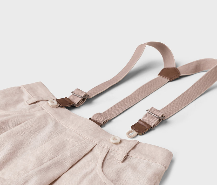 Egy bézs színű szövetnadrág közeli képe fehér háttérrel, nadrágtartóval.