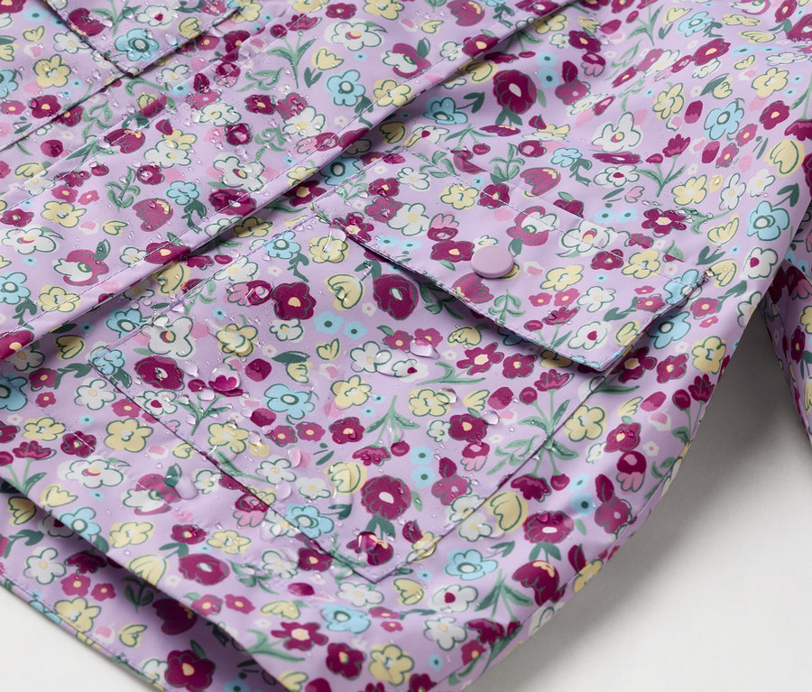 Egy gombokkal záródó, felvarrt zsebekkel ellátott, virágmintás lila esőkabát közeli képe.