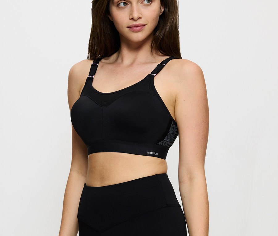 Nő fekete TRIUMPH Triaction Control Lite W01X kicsinyítő sportmelltartóban és fekete leggingsben, jobbra néz.
