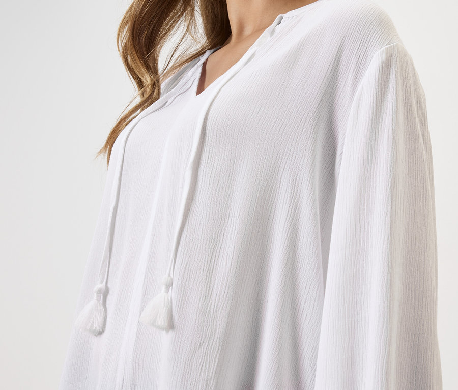 Közeli kép egy zsinóros, fehér blúzt viselő nőről.