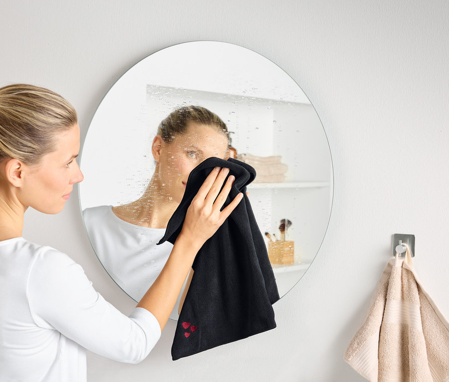 Egy nő egy párás, kerek tükröt tisztít egy fekete törlőkendővel.