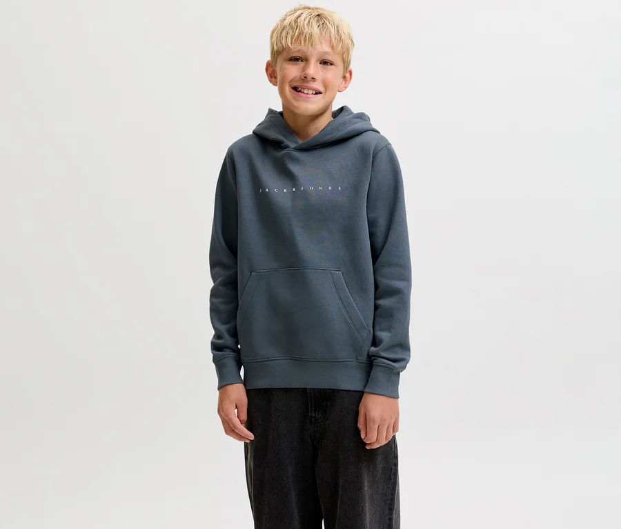 Mosolygó fiatal fiú sötétszürke Jack&Jones Star kapucnis szabadidőfelsőben, kenguruzsebbel és sötét nadrágban.