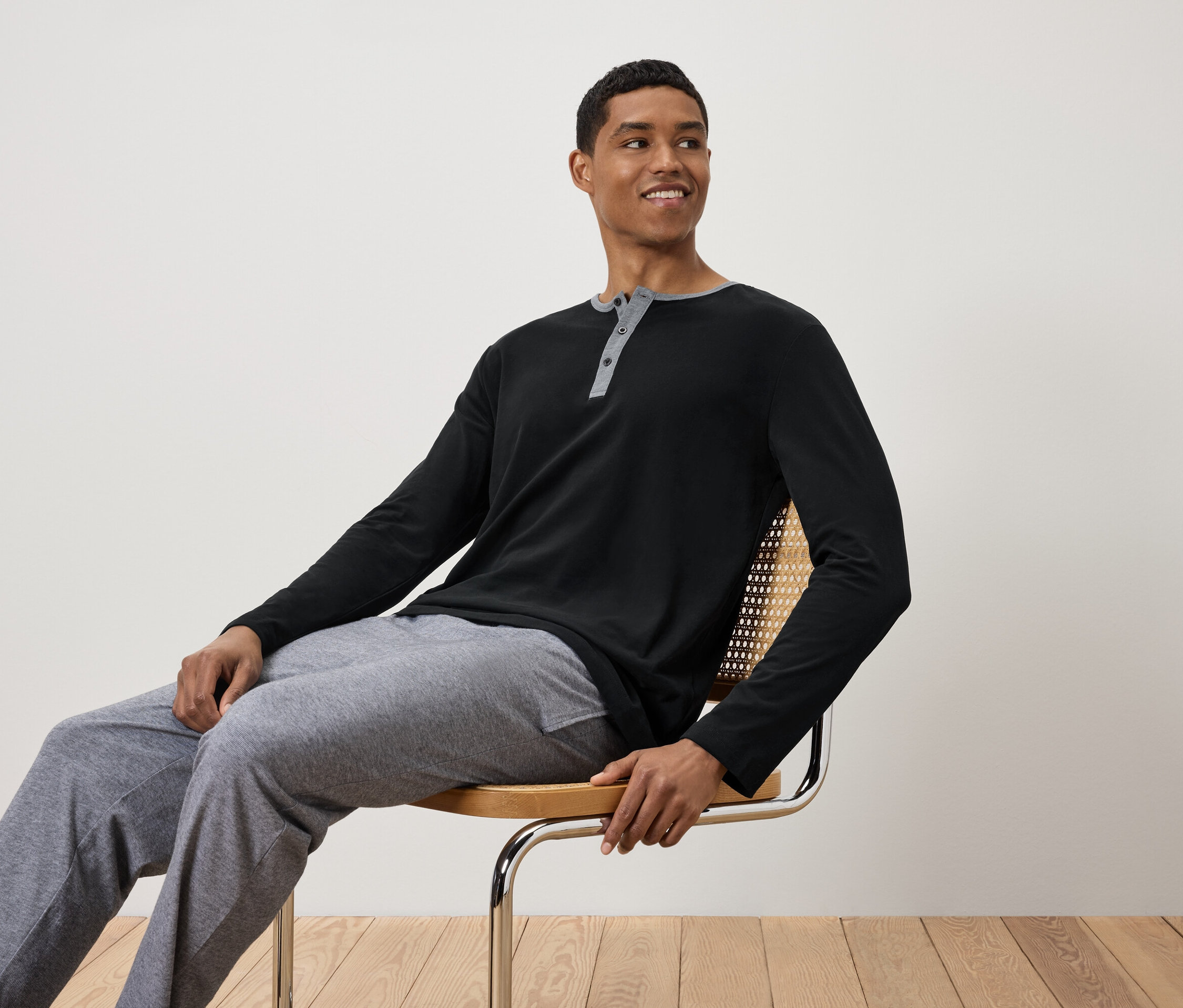 Férfi ül egy széken, fekete hosszú ujjú inget és szürke melegítőnadrágot visel.