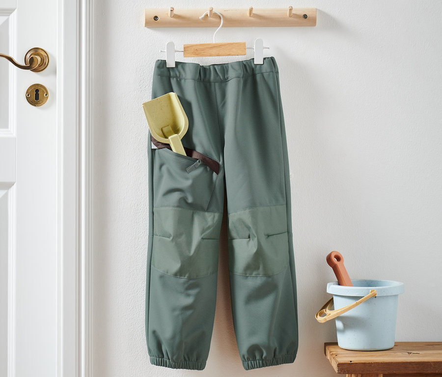 Egy softshell nadrág lóg a falon, zsebében és mellette a széken játékokkal.