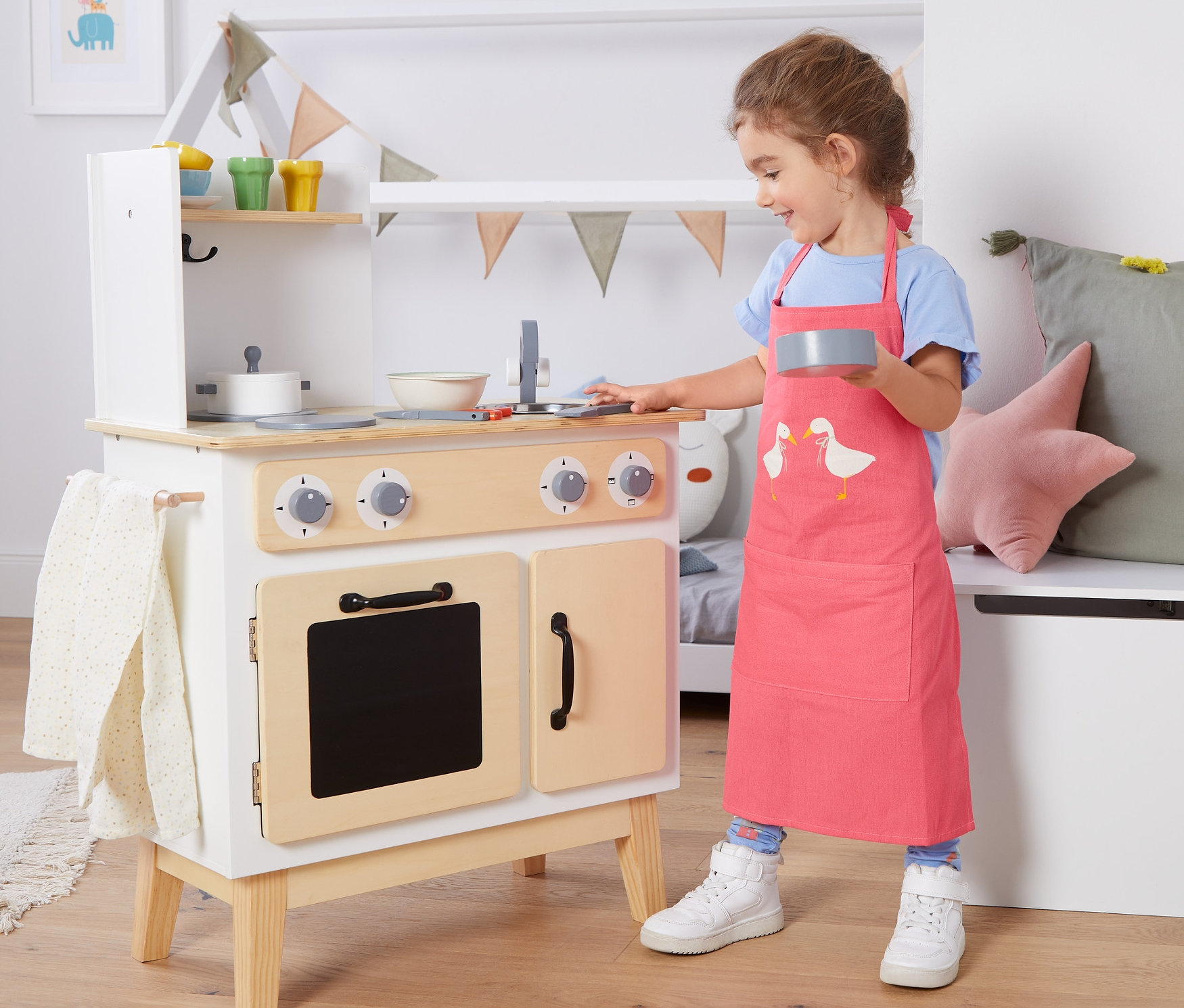 Kislány játszik a játékkonyhával, és gyerek konyhai kötényt visel.