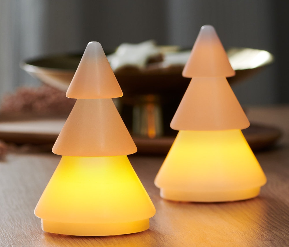 Két LED-es valódi viaszfenyő áll egy fa asztalon. A háttérben egy ablak látható.