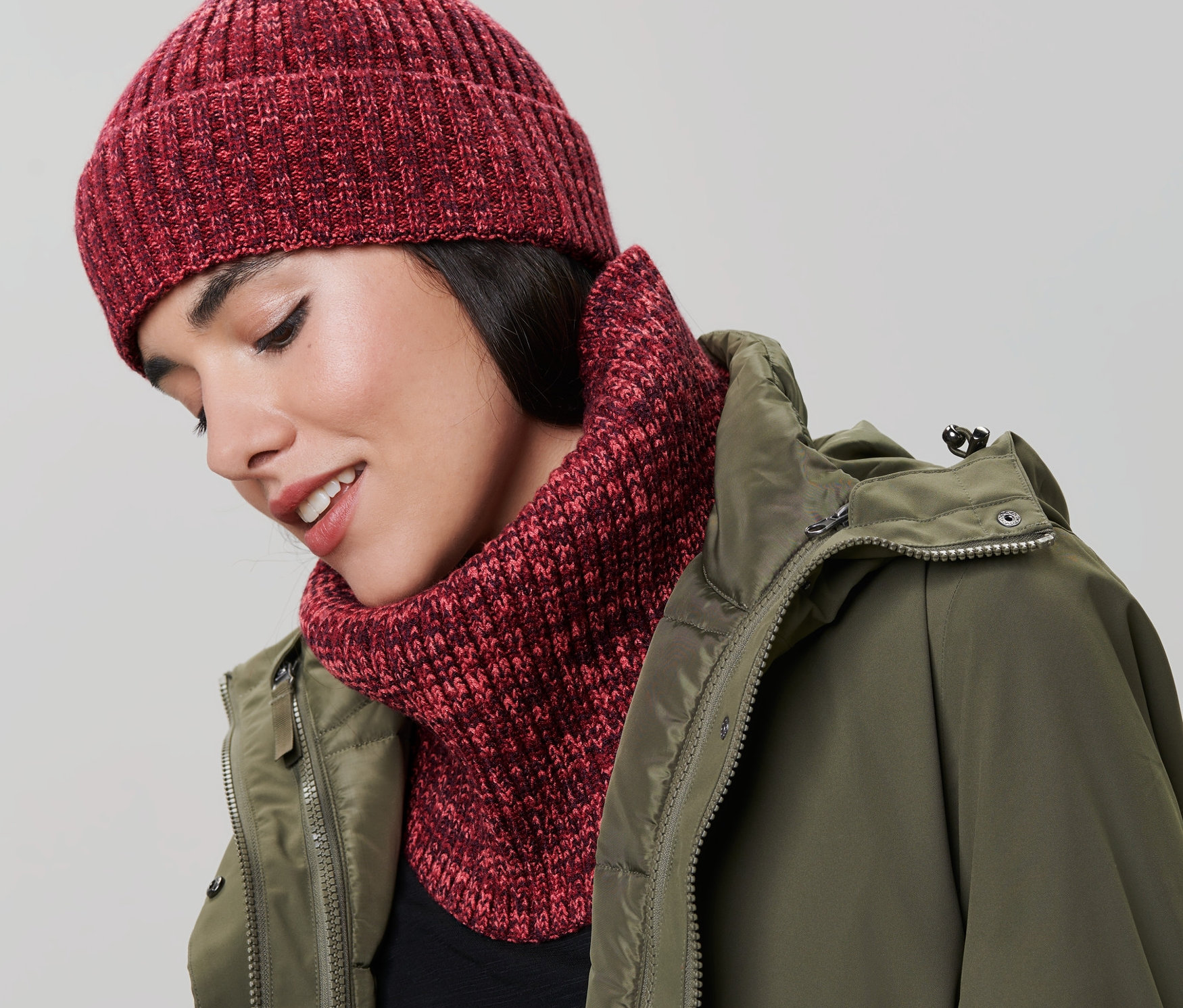 Nő kötött csősálat és sapkát visel. Zöld kabátot visel.