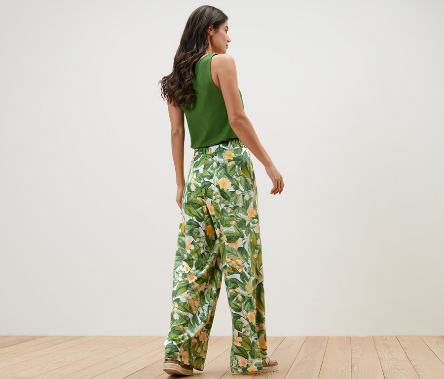 Nő pózol zöld felsőben és nyomott mintás palazzo nadrágban.