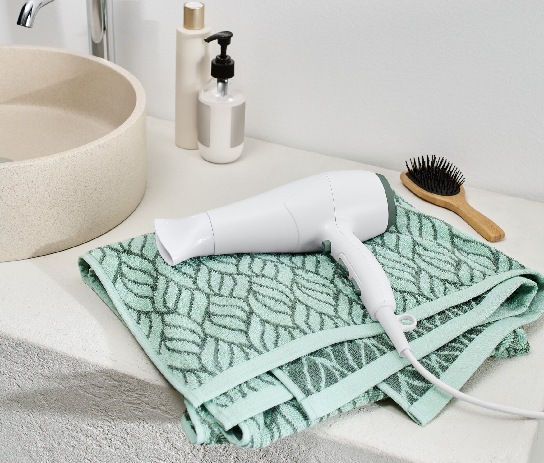 Egy fehér ionos hajszárító fekszik egy zöld törölközőn a fürdőszobában.