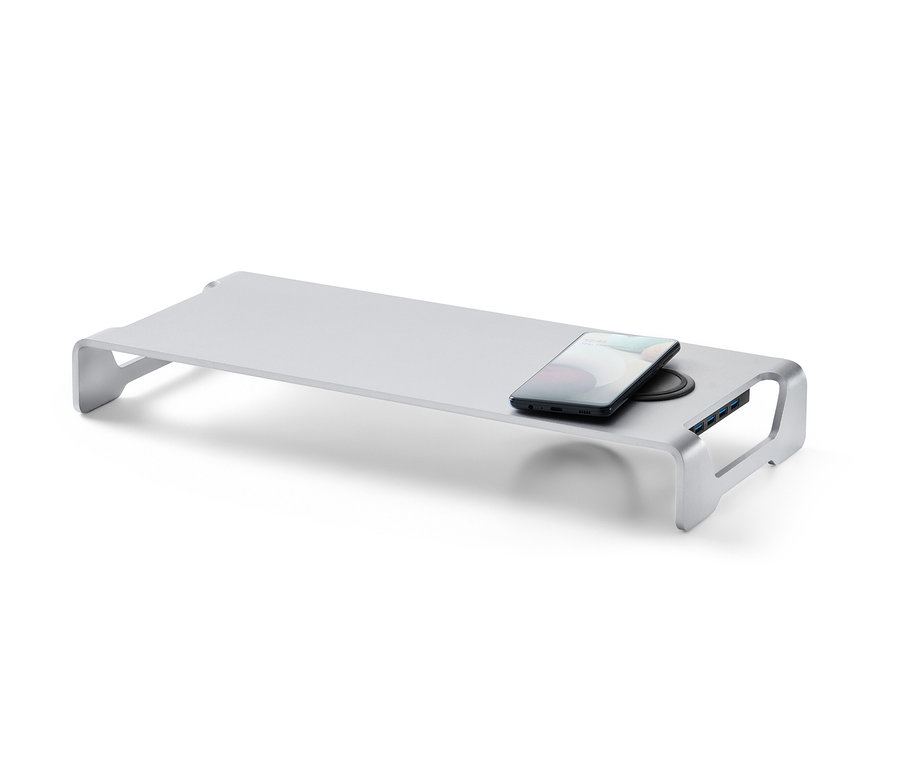 Ezüst monitorállvány vezeték nélküli töltővel és USB hubbal. A töltőn egy mobiltelefon van.