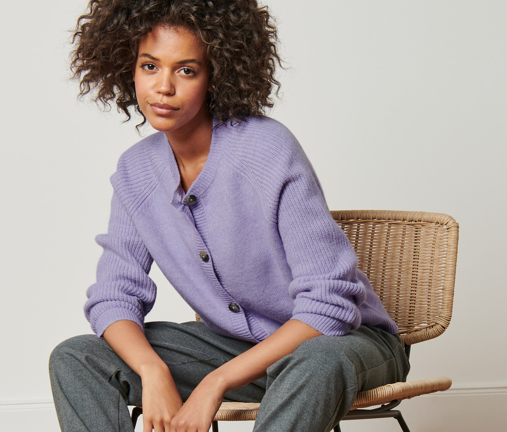 Nő ül egy széken, és lila kötött kardigánt visel.