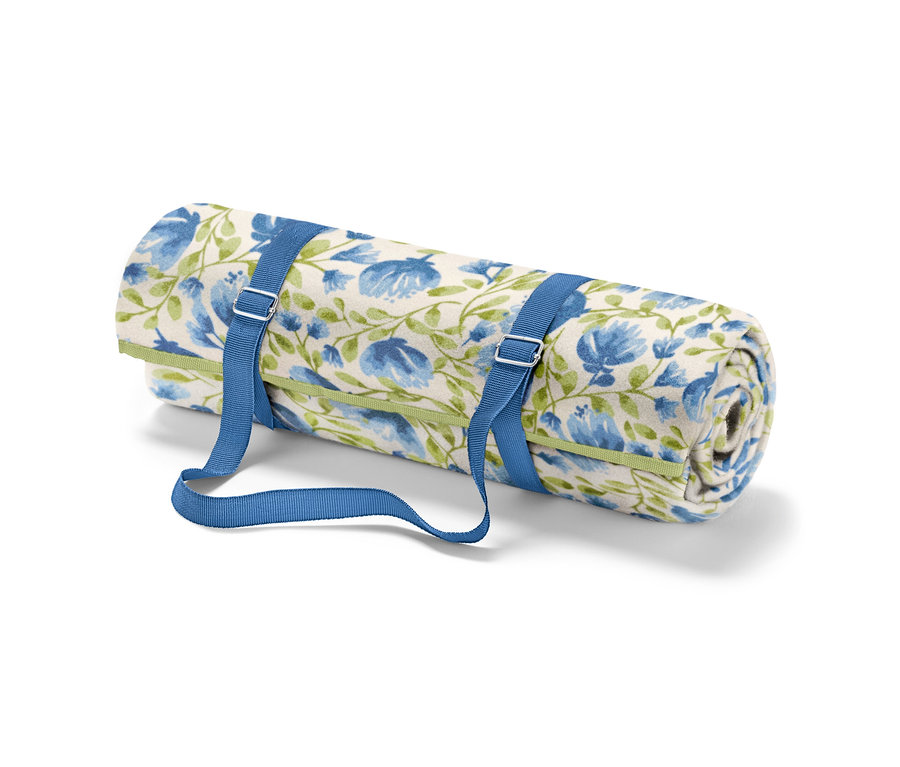 Egy feltekert kis pikniktakaró kék virágokkal és zöld szárakkal, kék pántokkal rögzítve.