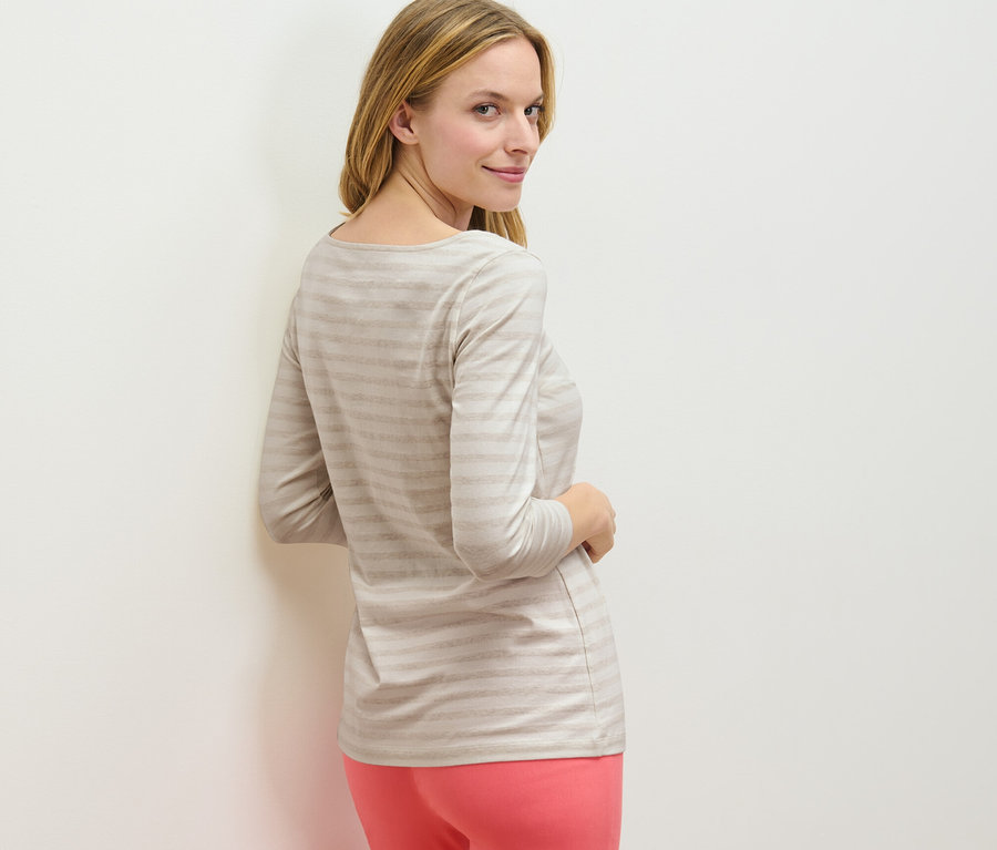 Egy nő a válla fölött hátra néz, és egy 3/4-es ujjú, csíkos felsőt visel.