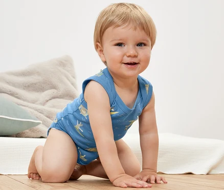 Mosolygó csecsemő térdelve kék, mintás 2 kisgyerek body-t visel.