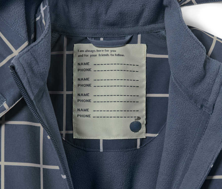 Egy kockás kisgyerek softshell kezeslábas részlete, név és telefonszám címkével.