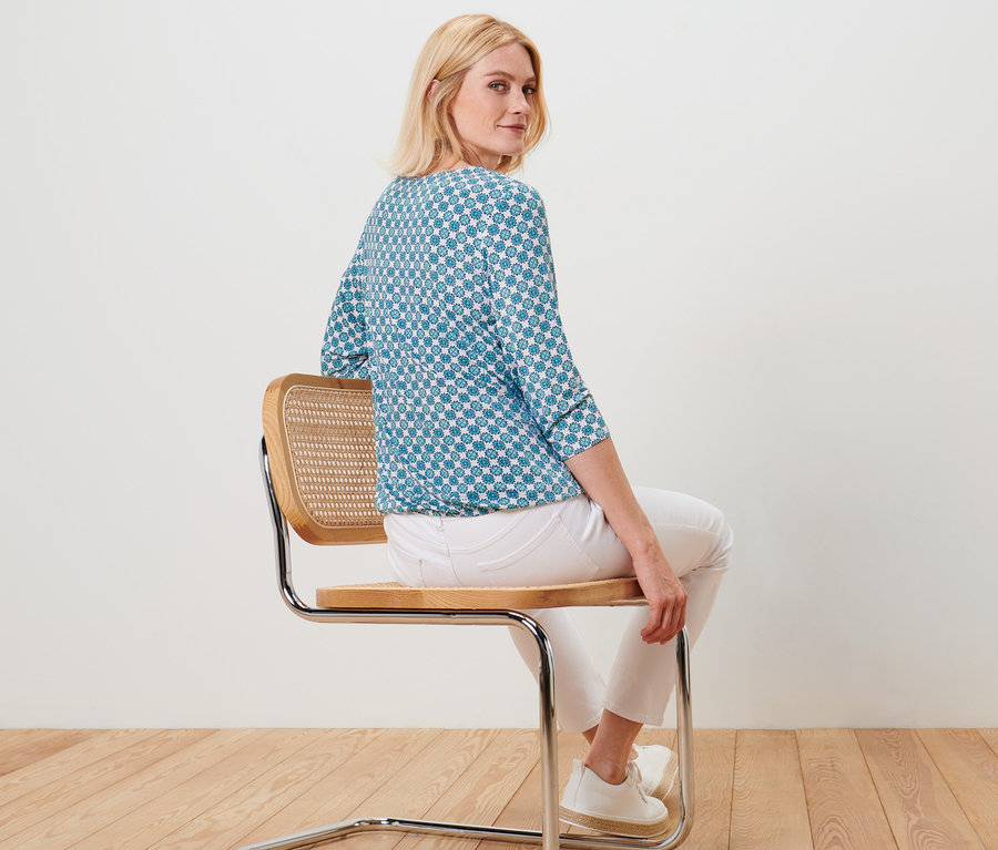 Nő ül egy széken, nyomott mintás női blúzt visel.