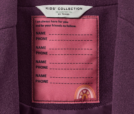 Egy kislány szövetkabát részlete a KIDS' COLLECTION címkével, rajta hely a név és a telefonszám számára.