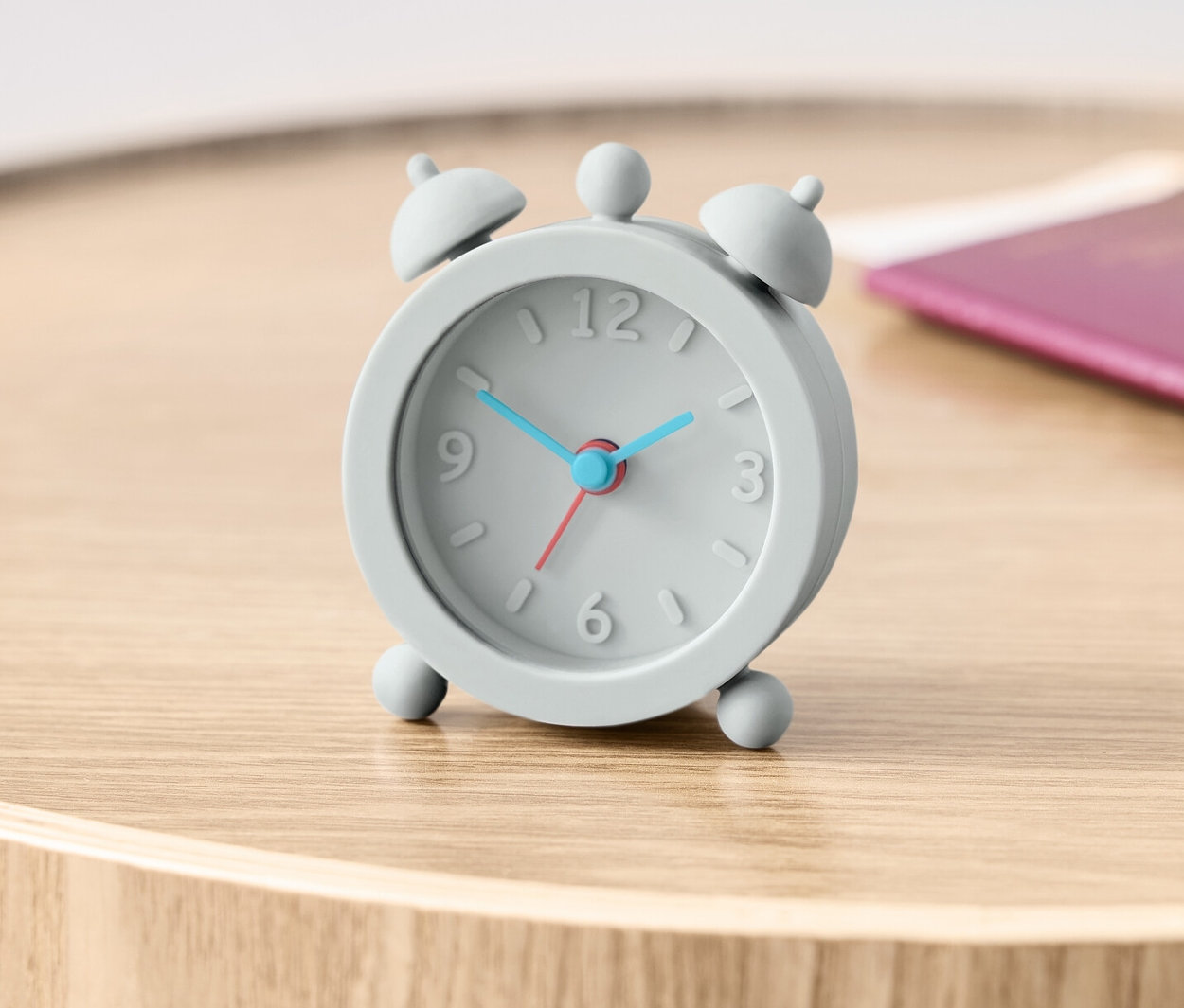 Szürke úti ébresztőóra egy fa asztalon egy útlevél mellett.