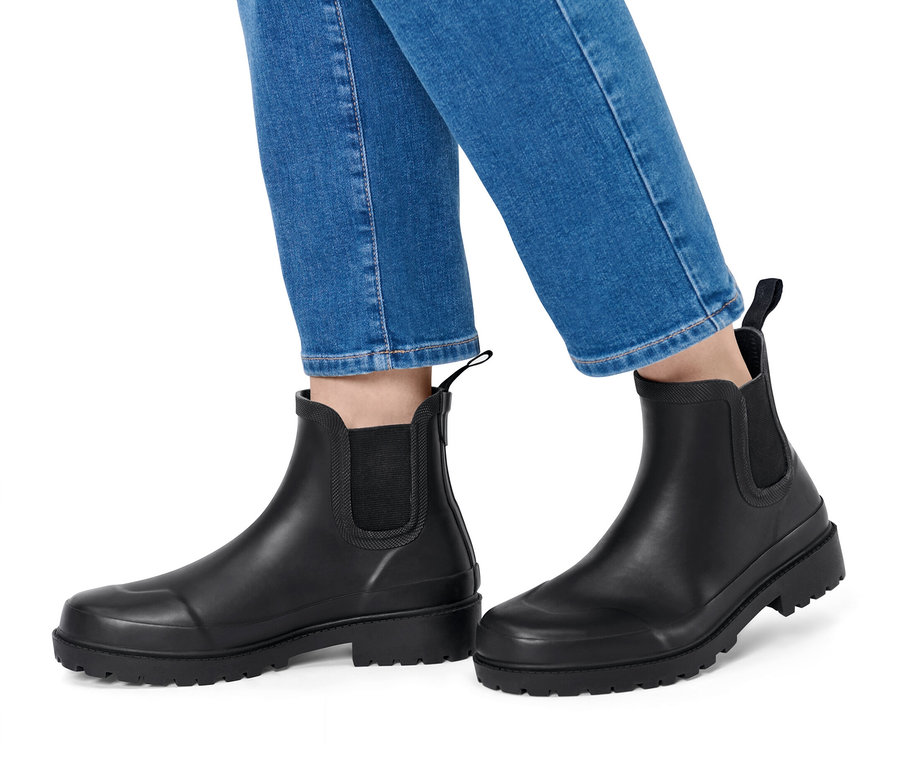 Kék farmerben és fekete gumicsizmában lévő lábak fehér háttéren.