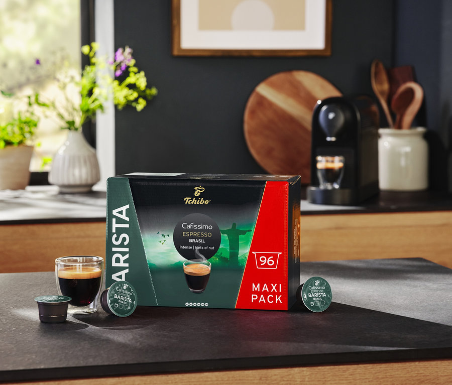 Az asztalon egy csomag Cafissimo BARISTA Espresso Brasil kapszula, egy pohár eszpresszó és egy kávéfőző található.