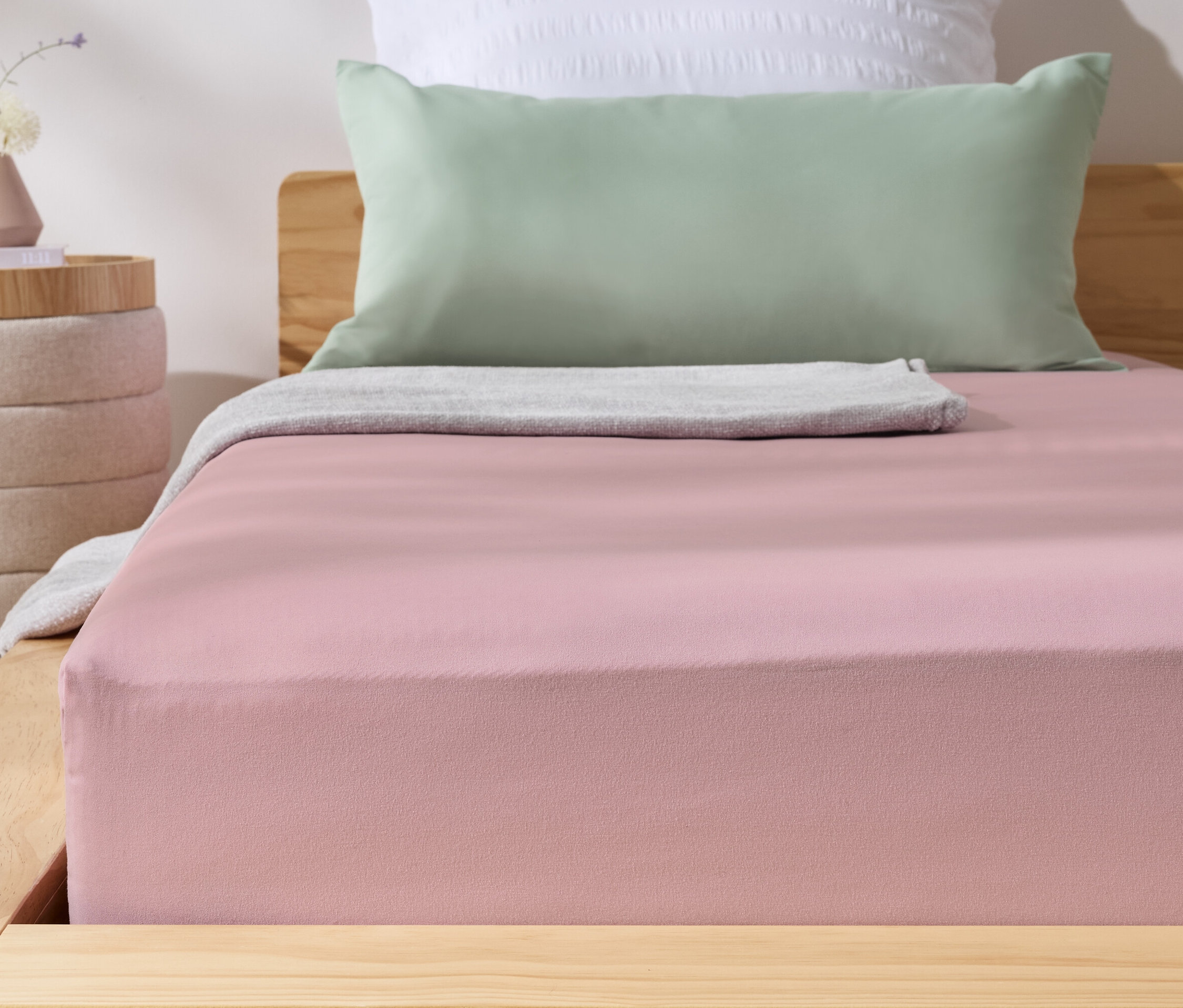 Rózsaszín mikroszálas gumis lepedő egy ágyon. Mellette egy éjjeliszekrény egy vázával.