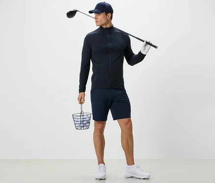 Férfi sötétkék funkcionális felsőben golflabdákkal teli kosarat és golfütőt tart.