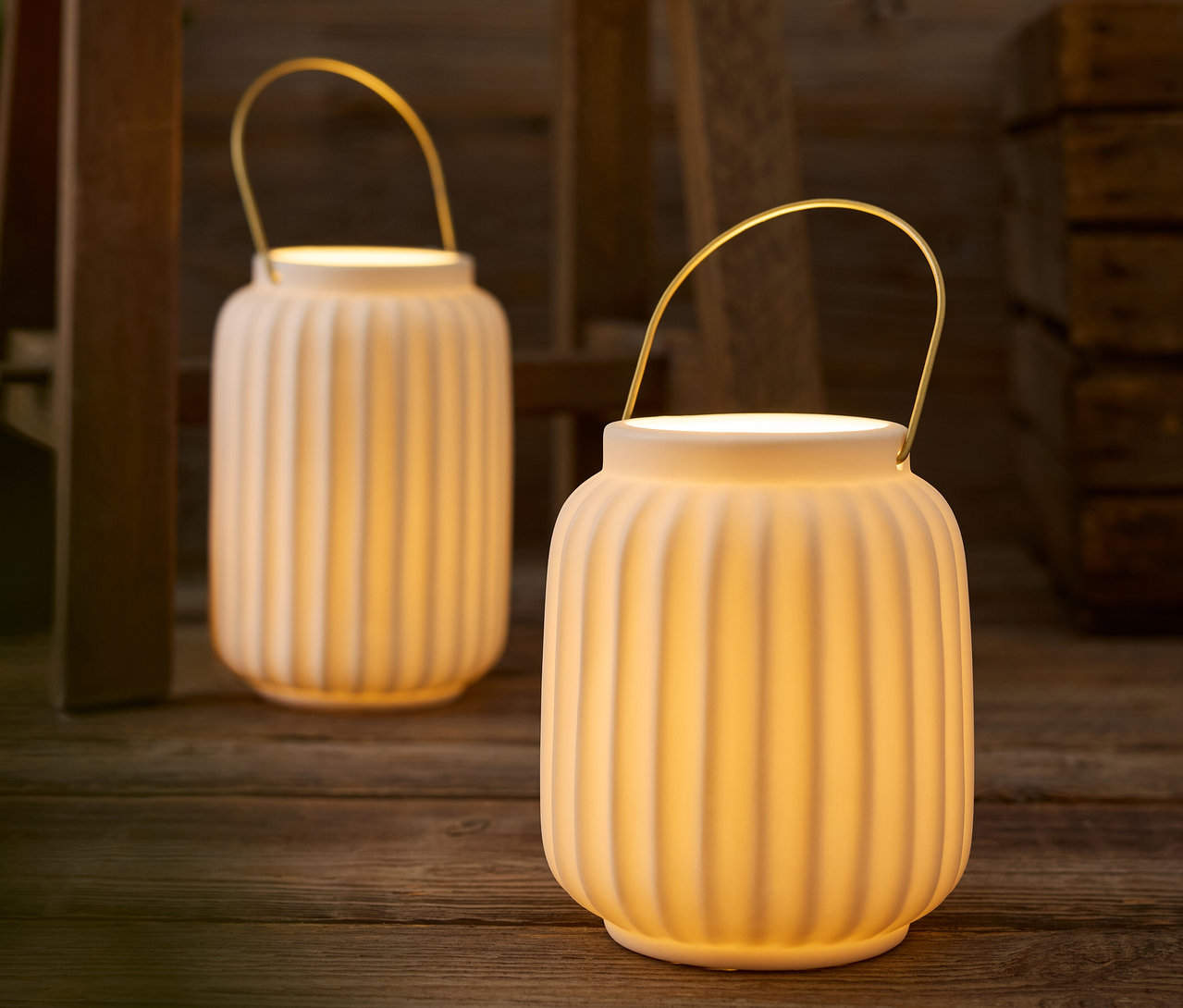 Két fehér lámpás arany fogantyúval egy fa asztalon.