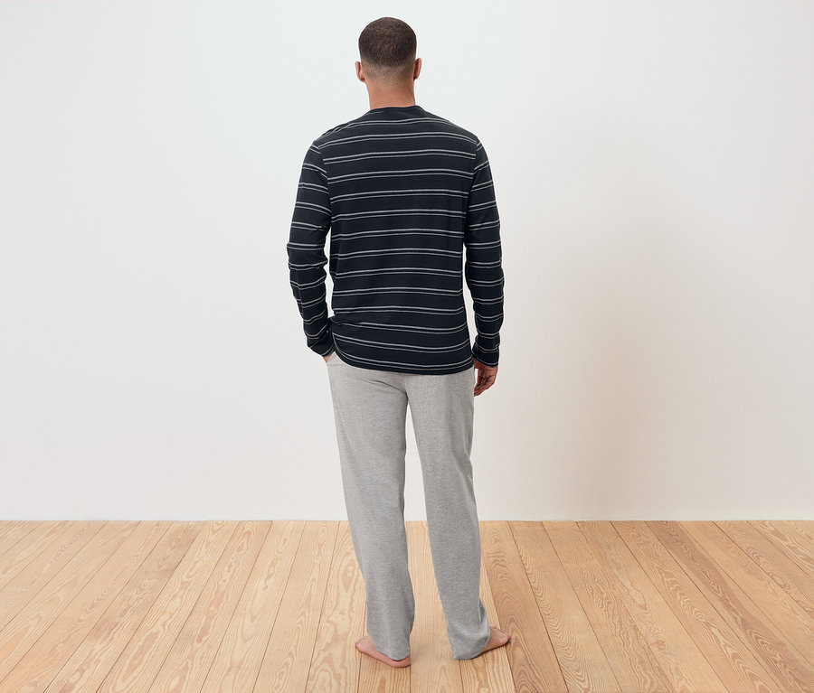 Egy férfi háttal a kamerának, csíkos hosszú ujjú inget és szürke melegítőnadrágot visel.