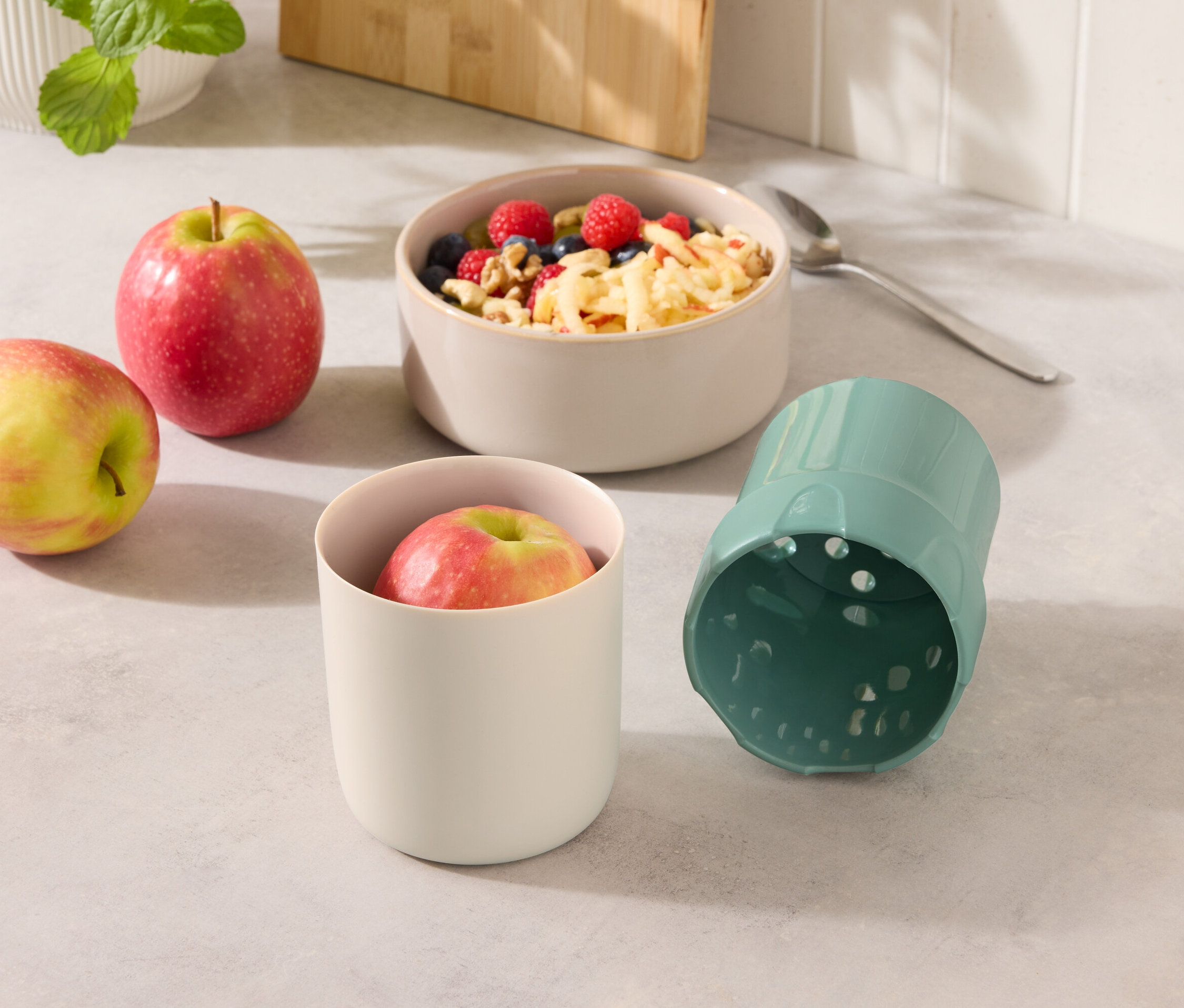 Két alma egy müzlis tál és egy almás pohár és egy kék pohár mellett.