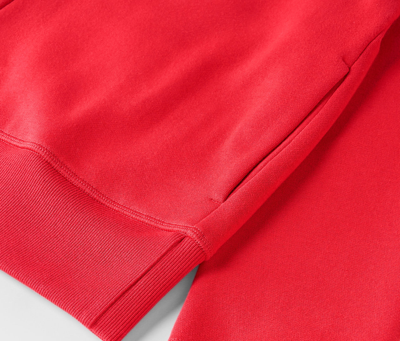 Egy piros, bordázott szegélyű kapucnis pulóver részlete.