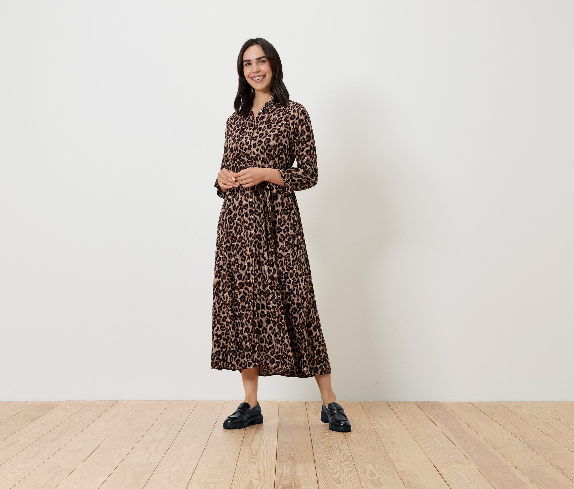 Egy nő mintás, hosszú ujjú ruhában és fekete cipőben pózol.