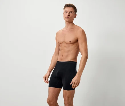 Egy férfi szabad felsőtesttel fekete boxeralsóban áll egy fehér háttér előtt.