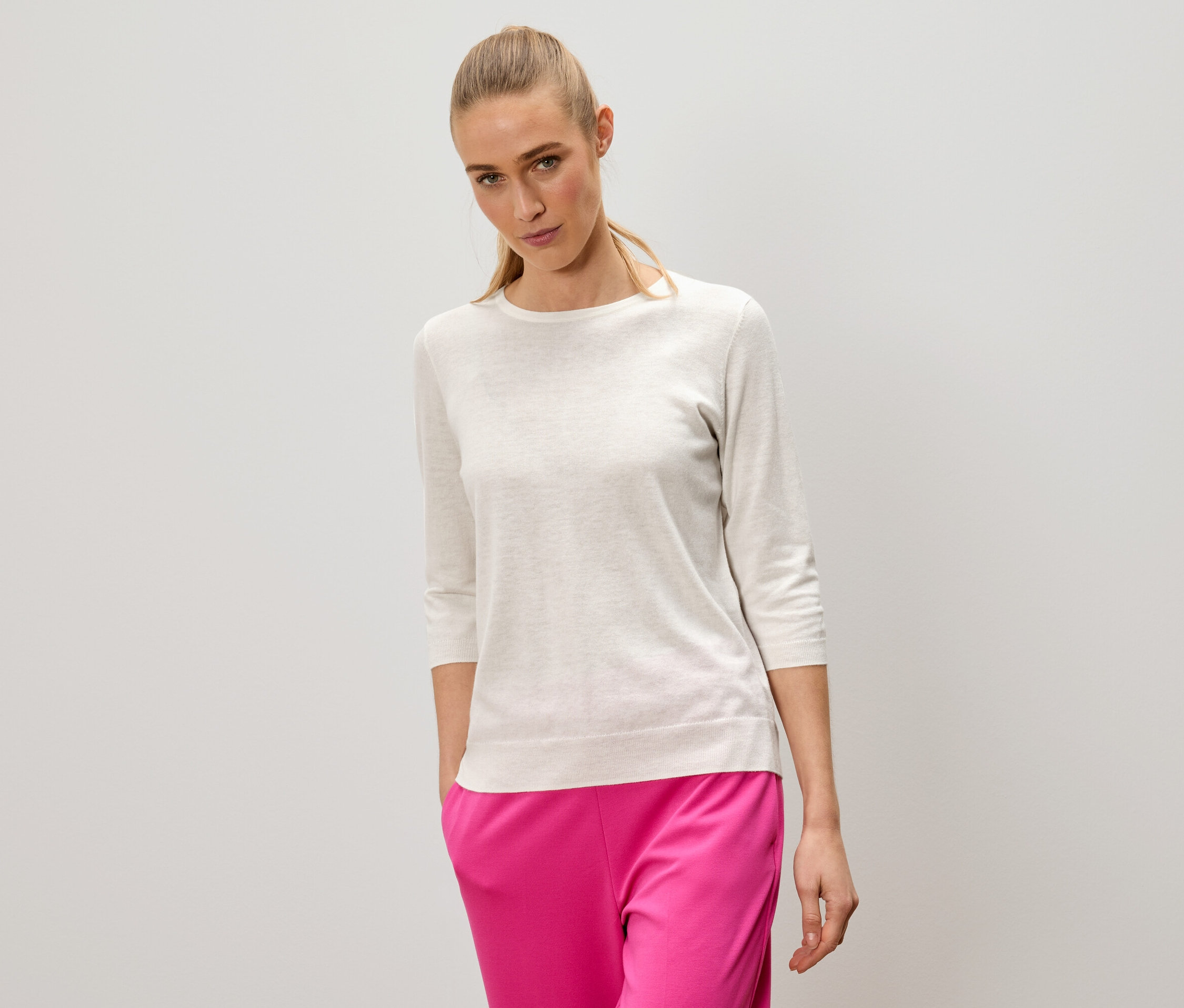 Egy szőke hajú nő világos pulóvert és rózsaszín nadrágot visel.