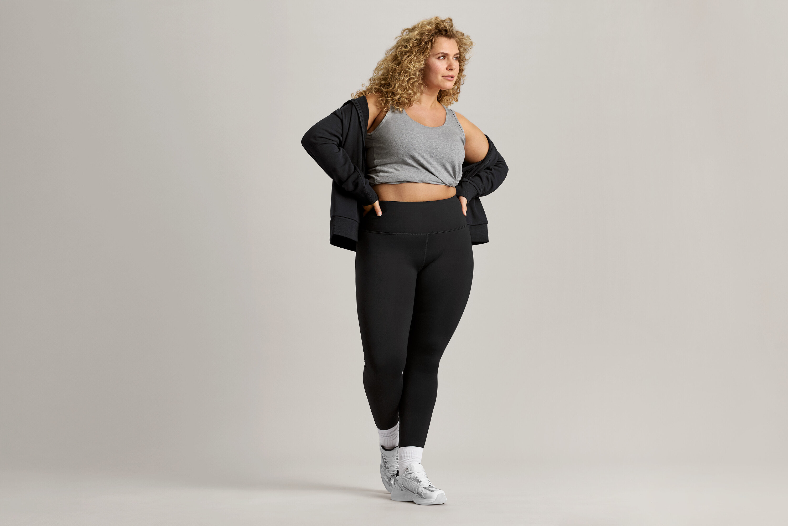 A göndör hajú nő szürke trikót, fekete kabátot és fekete leggingset visel.