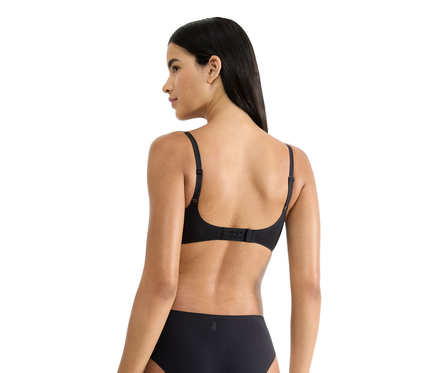 Hátulnézet egy hosszú, sötét hajú nőről, aki fekete melltartót és alsóneműt visel.