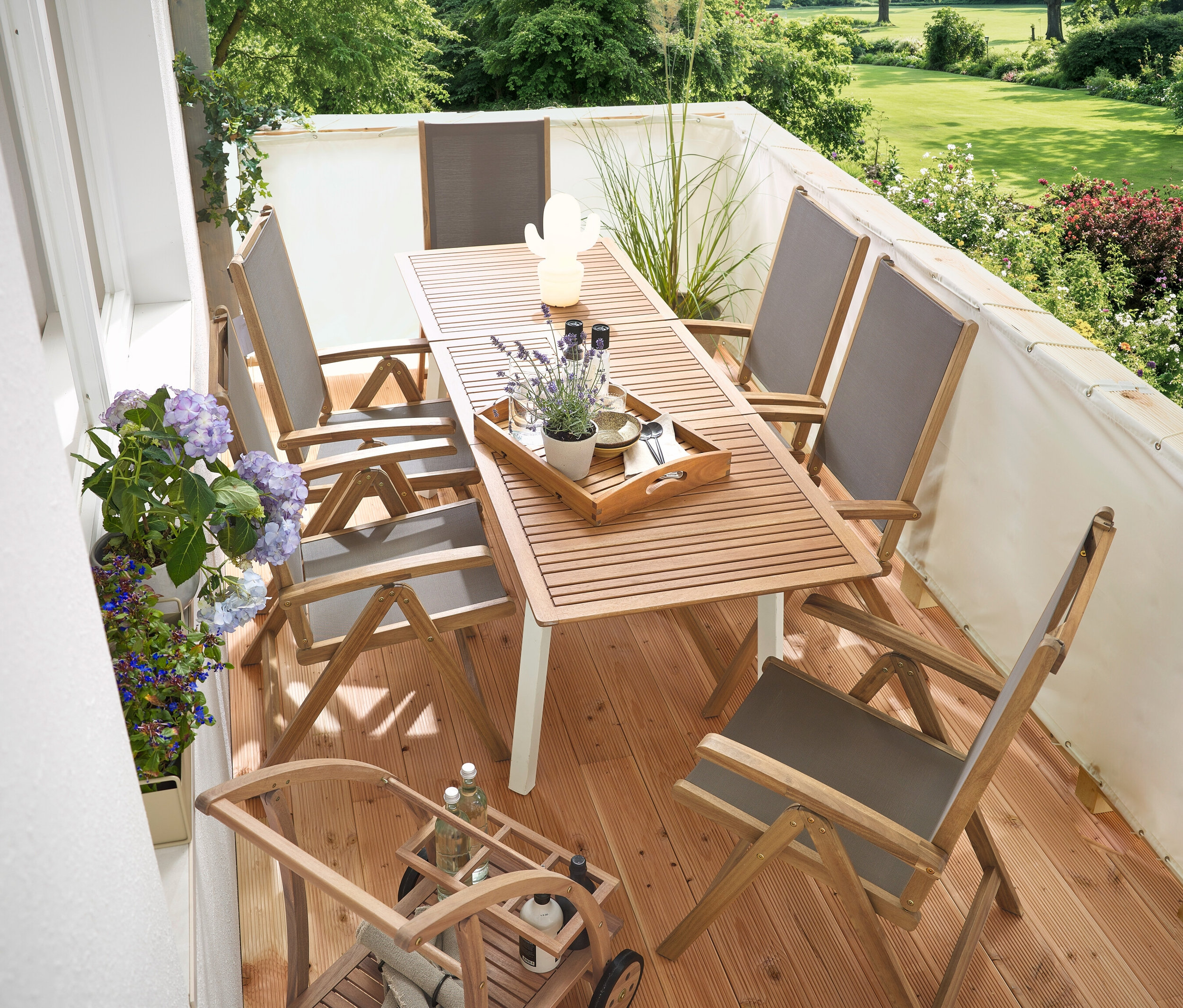 Egy erkélyen egy keskeny, kihúzható »Liska« kerti asztal, egy krémszínű erkélyre való belátásgátló és szélvédő, egy barwagen mit abnehmbarem Tablett és egy LED kültéri akkumulátoros asztali lámpa, kaktusz található.