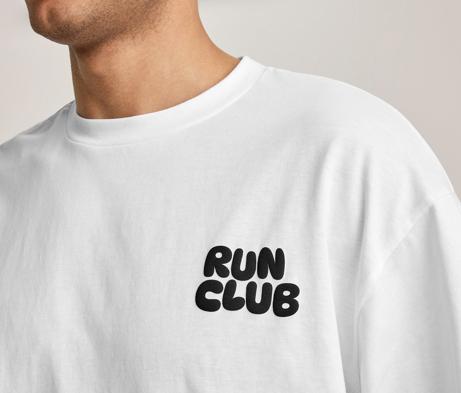 Egy személy fehér sportfelsőt visel „RUN CLUB” felirattal a mellkasán.