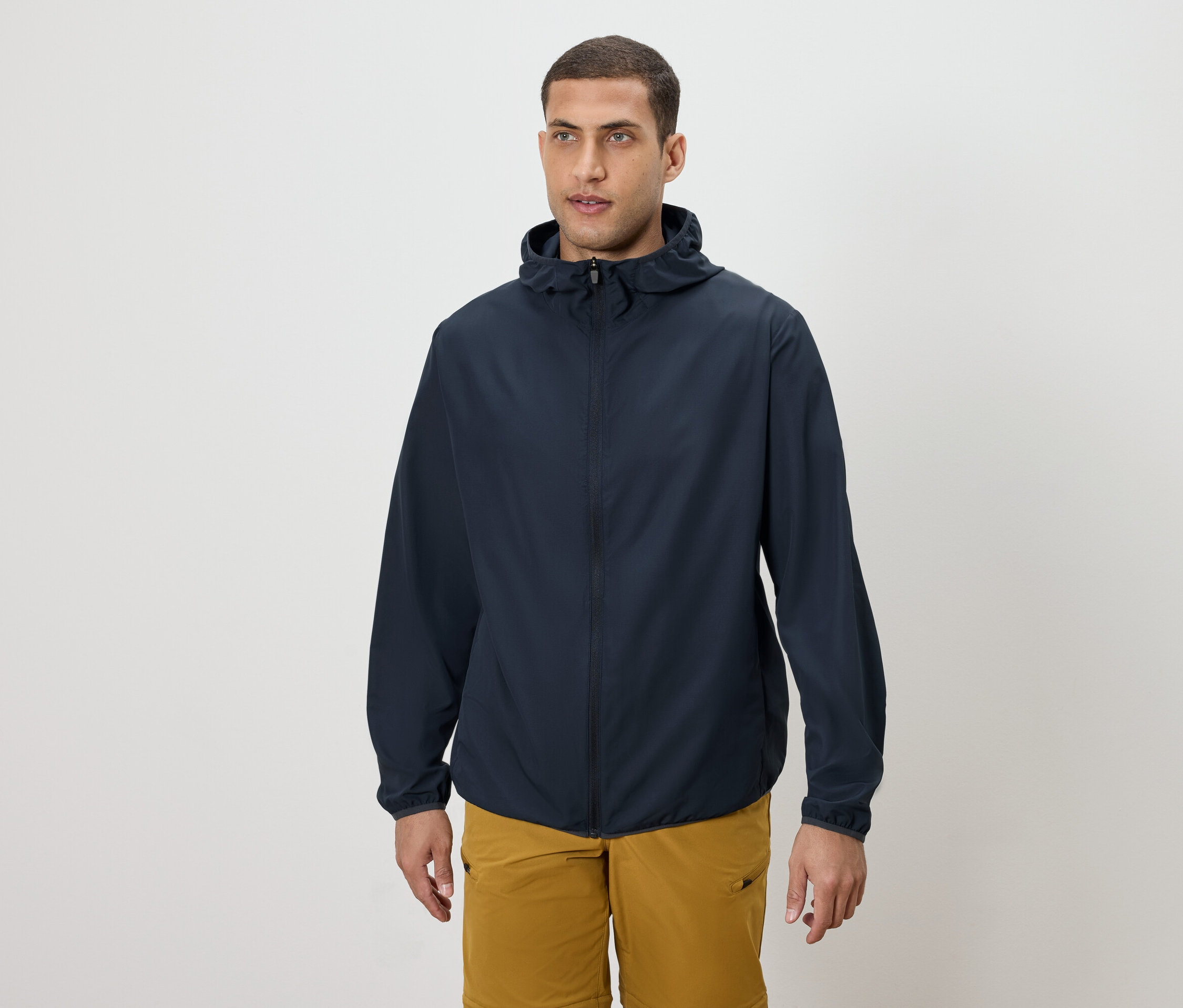 Férfi sötétkék kapucnis kabátot és aranyszínű rövidnadrágot visel.