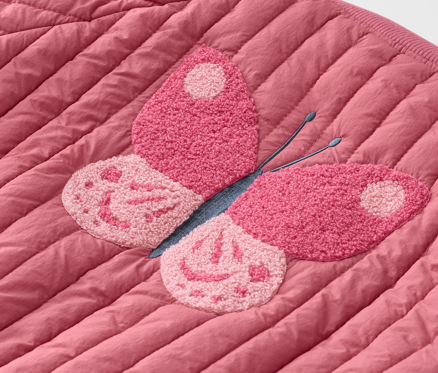 Egy rózsaszín, steppelt kabát közeli felvétele rózsaszín pillangó hímzéssel.