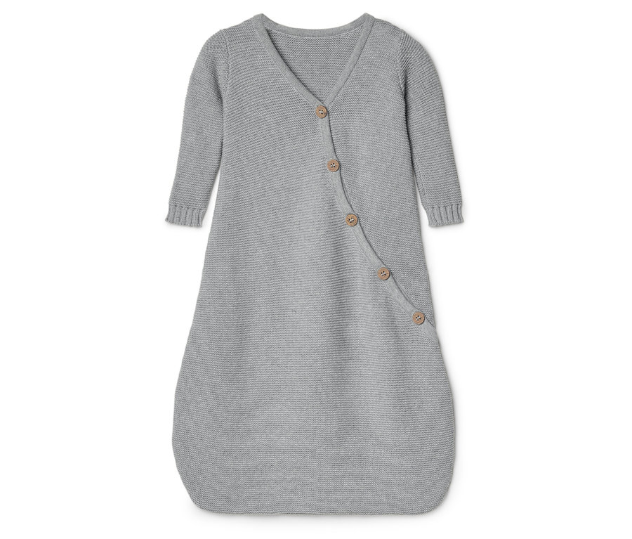 Egy szürke, kötött, hosszú ujjú, gombos babahálózsák fekszik egy fehér felületen.