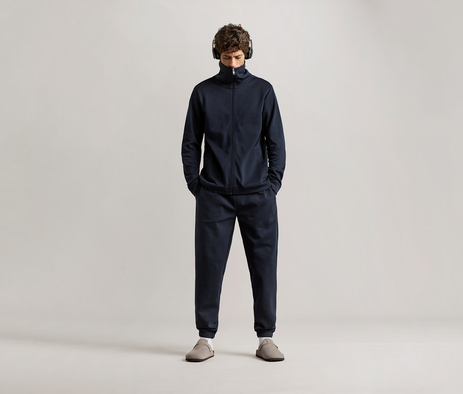 Férfi fejhallgatóval a fülén, sötétkék férfi szabadidő szettben.