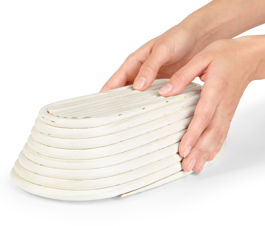 Két kéz egy ovális kenyérkelesztő kosarat tart.