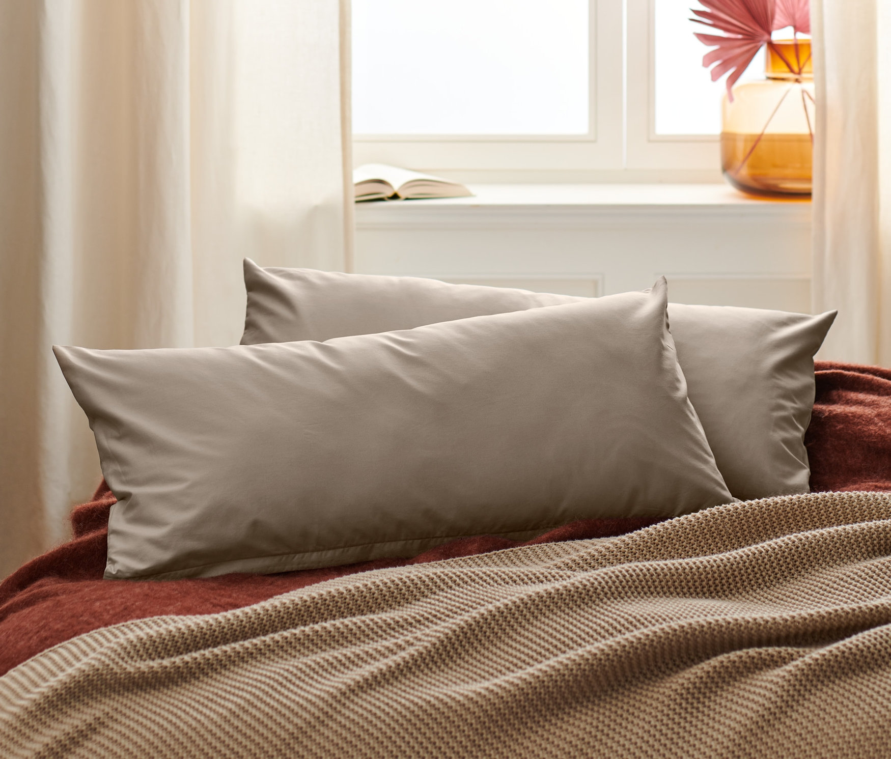 Két bézs perkál párnahuzat fekszik egy ágyon egy barna takaróval.