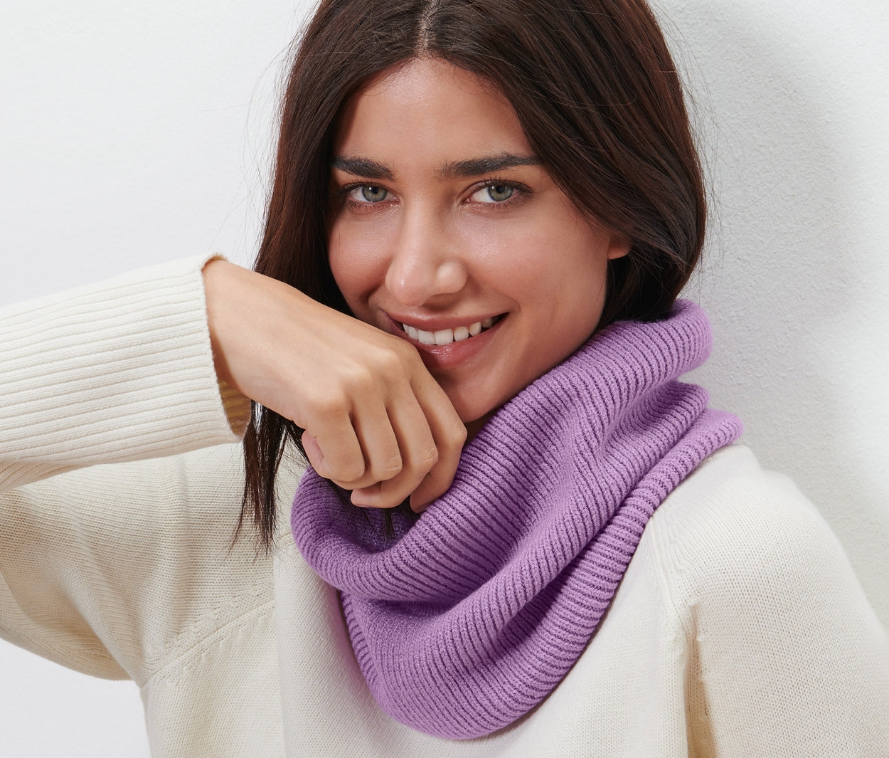 Barna hajú nő mosolyog, lila kötött csősálat visel.