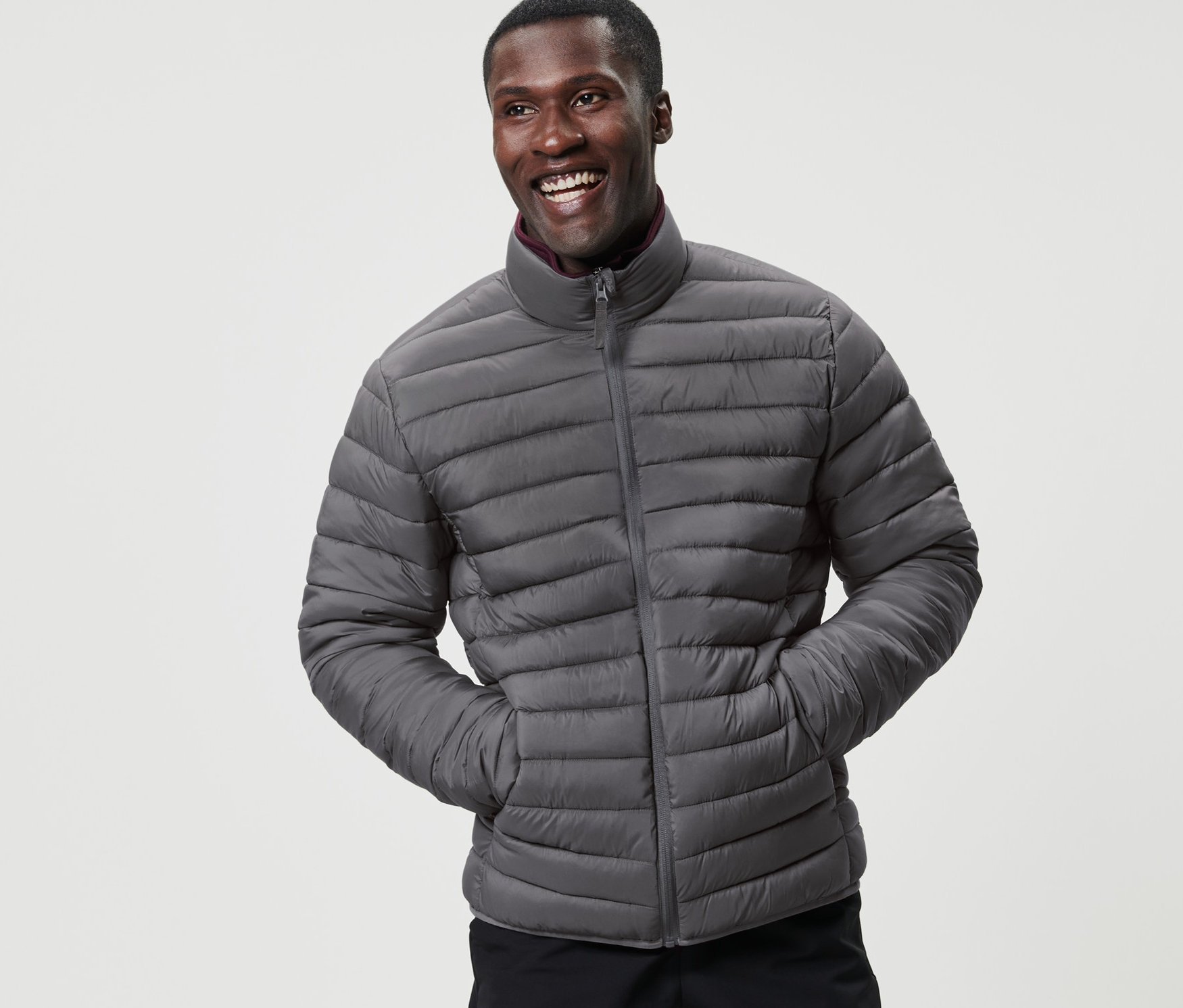 Egy mosolygó férfi szürke, összehajtható, steppelt dzsekiben pózol.