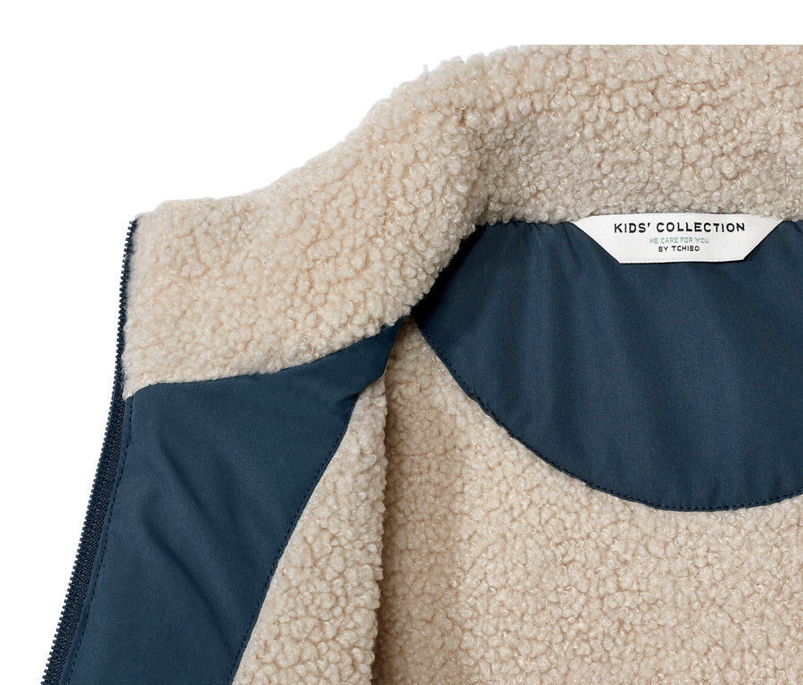 Egy gyerek steppelt mellény részlete, plüssbéléssel, a belső oldala kék.