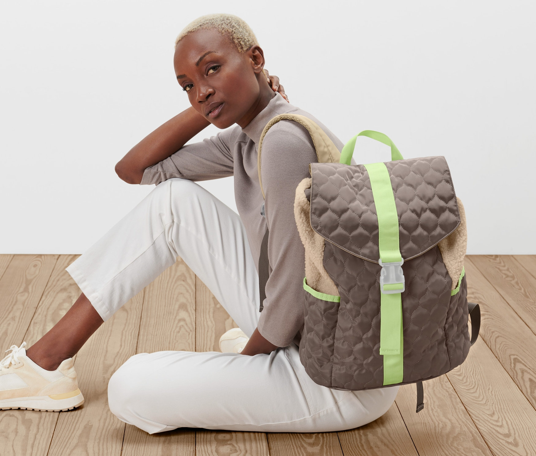 Nő ül a földön egy steppelt hatású hátizsák mellett.