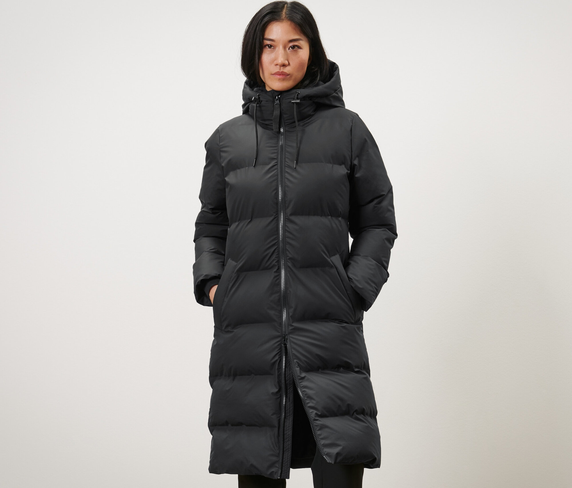 Nő visel egy hosszú, fekete női steppelt esőkabátot.